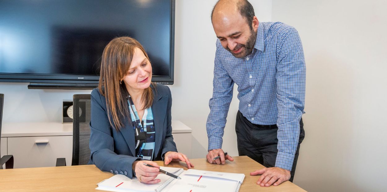 A man and a woman are looking at a document on a desk. 